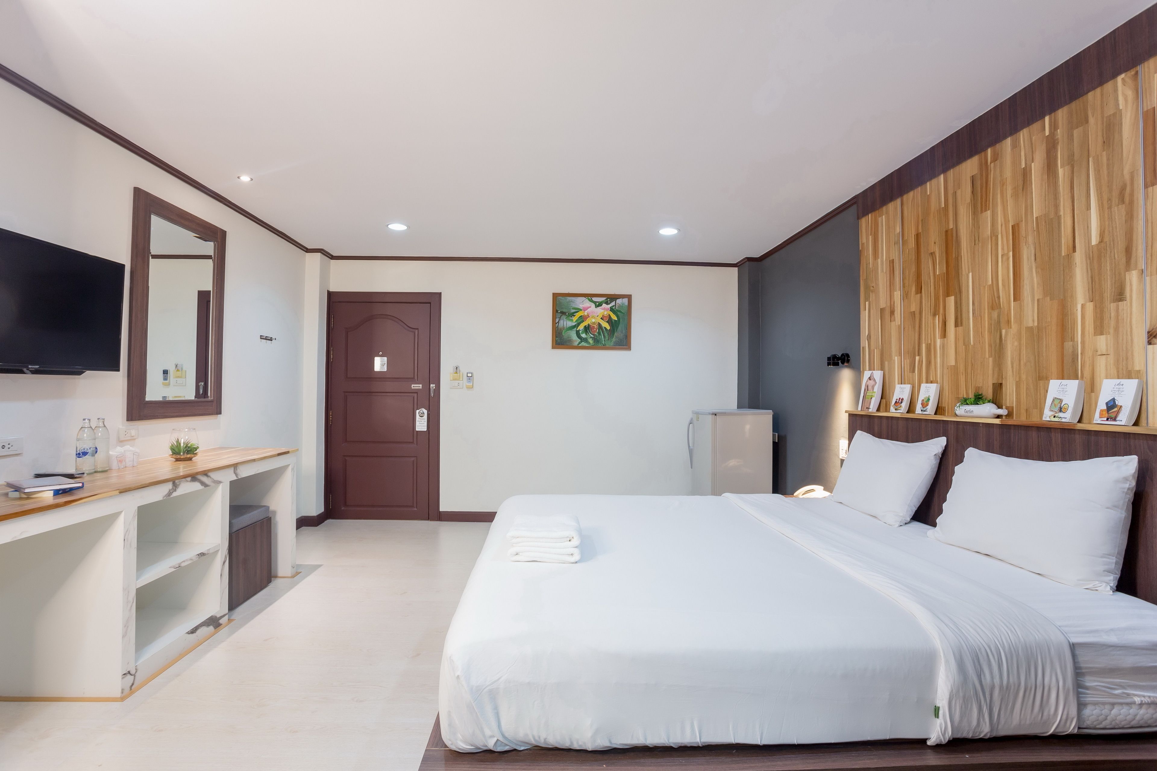 Una habitación de hotel moderna con una cama grande, un revestimiento de madera, un televisor de pantalla plana, un escritorio con espejo y una planta pequeña.