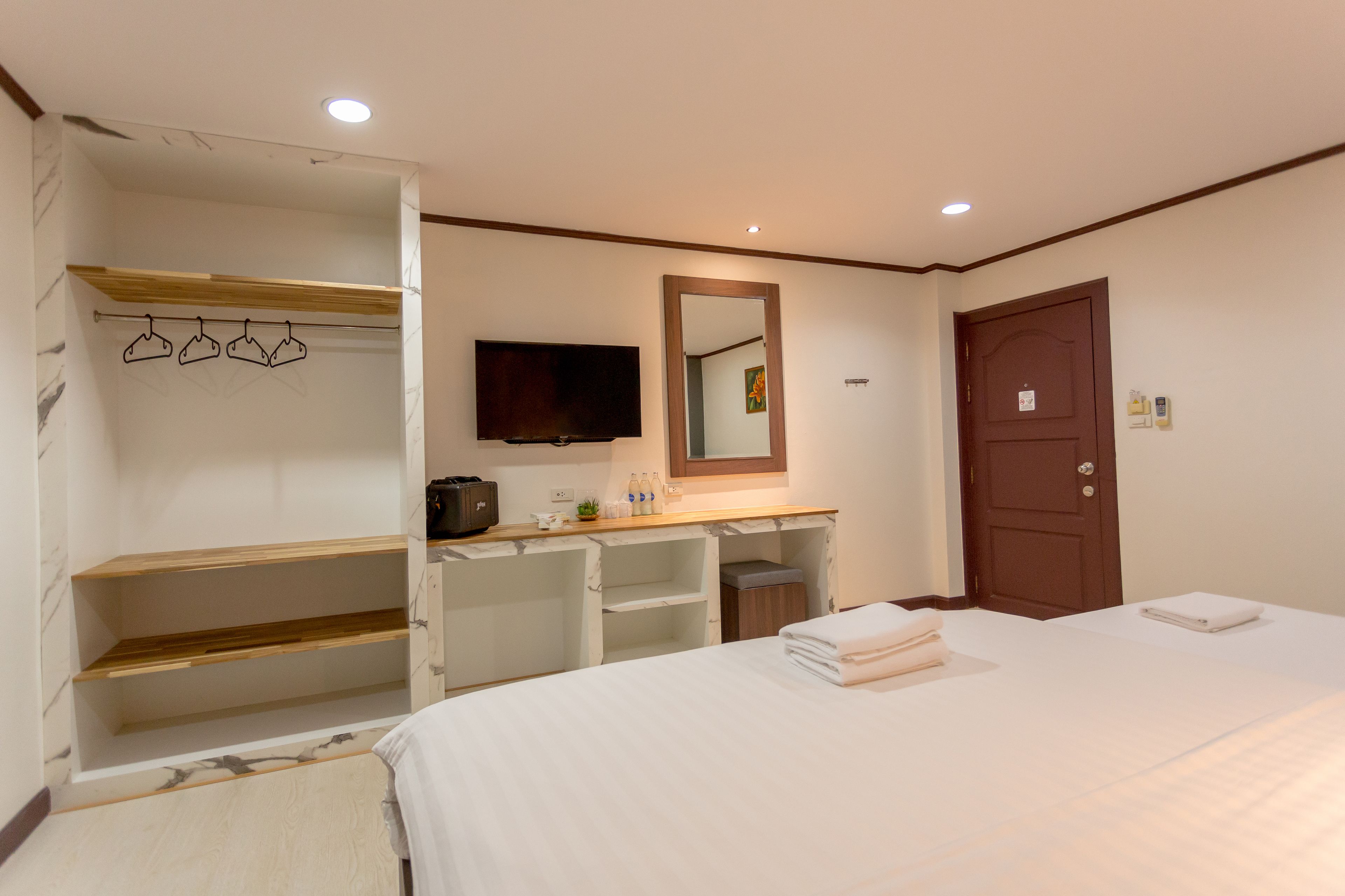 A hotel room with a bed, a TV, a mirror, a wooden shelf, and a desk with a chair.