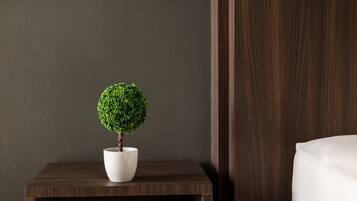 A small potted tree on a wooden nightstand next to a bed in a hotel room.