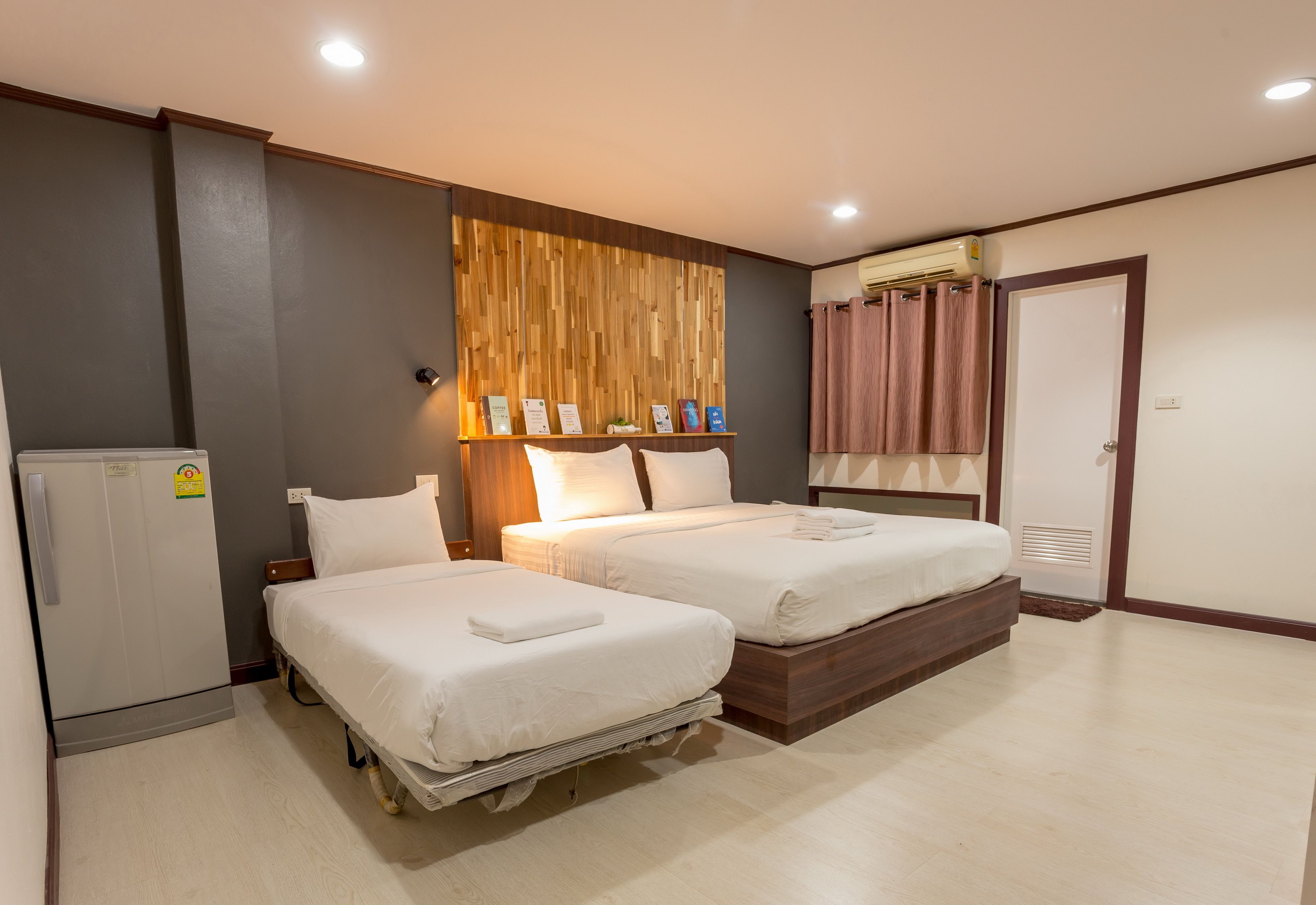 A hotel room with two beds, a wardrobe, a small fridge, and a wooden wall panel.
