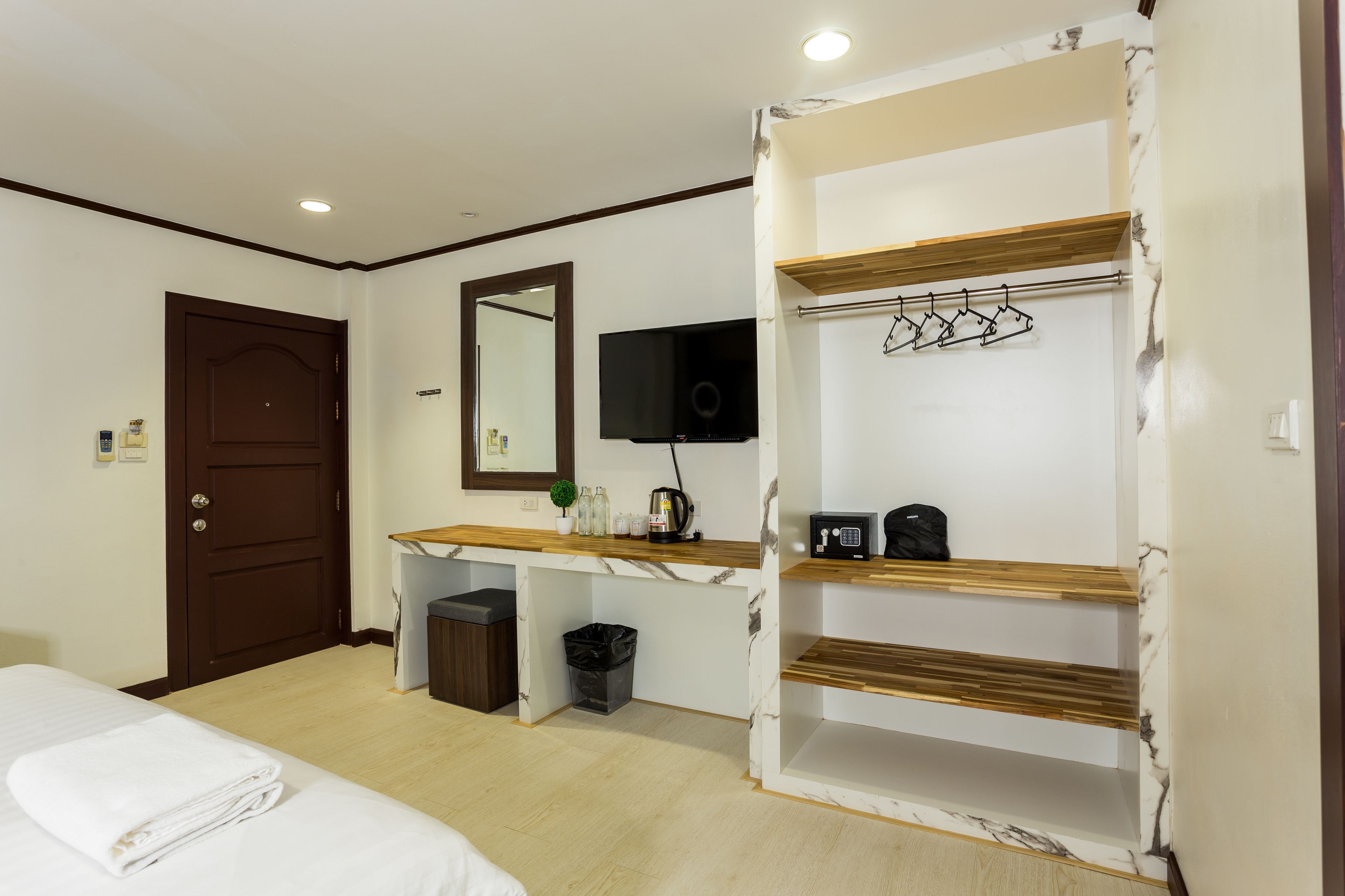 A hotel room with a bed, a desk with a mirror, a TV, and a shelf with a coat rack.