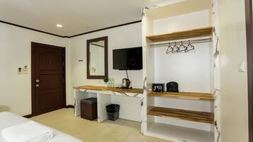 A hotel room with a bed, a desk with a mirror, a TV, and a shelf with a coat rack.