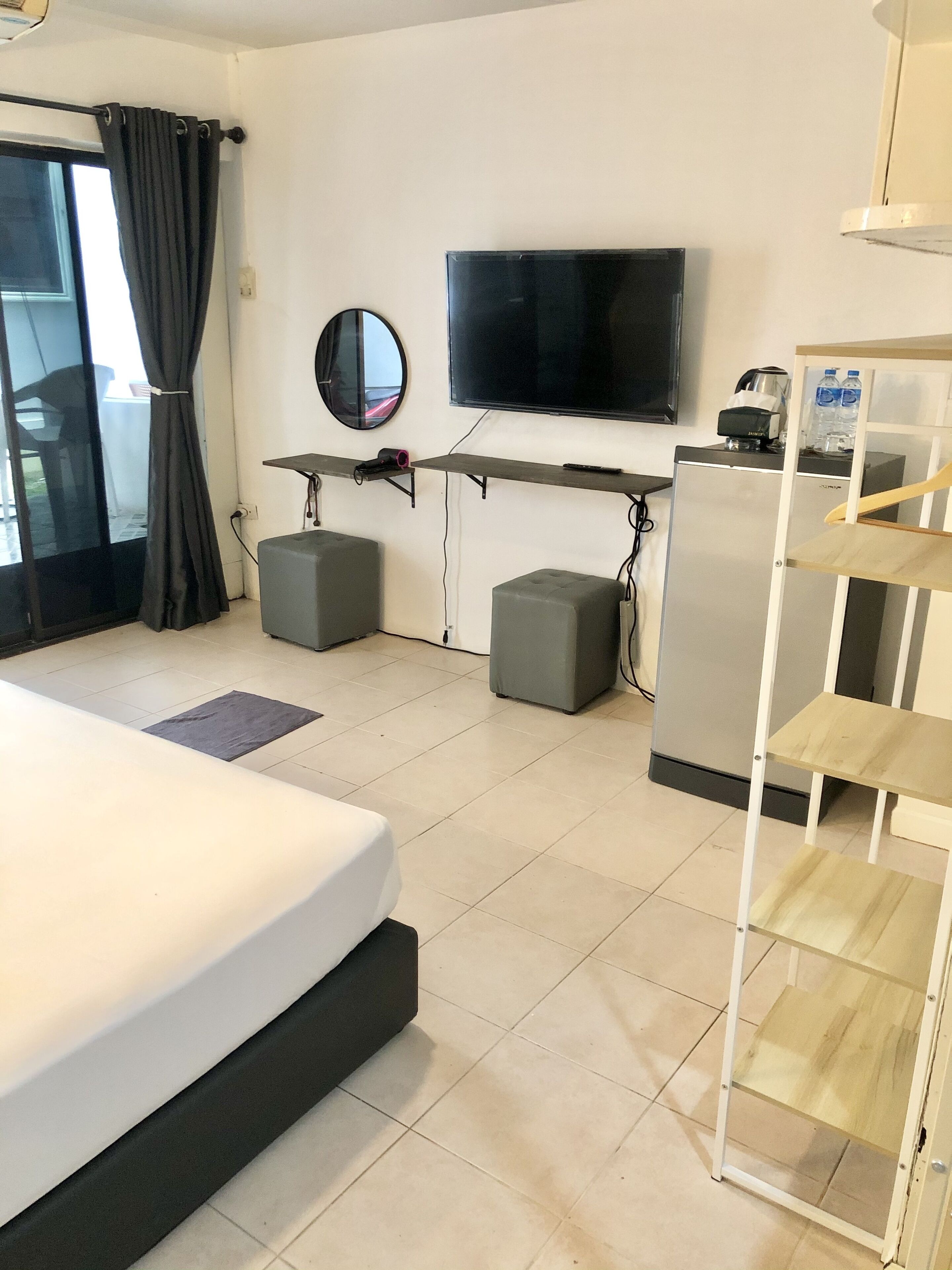 A hotel room with a bed, a flat-screen TV mounted on the wall, a small refrigerator, and a wooden shelf unit.