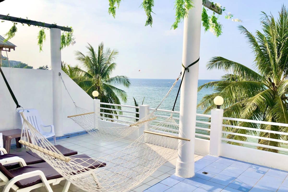 A rooftop terrace with a hammock, lounge chairs, and a view of the sea.