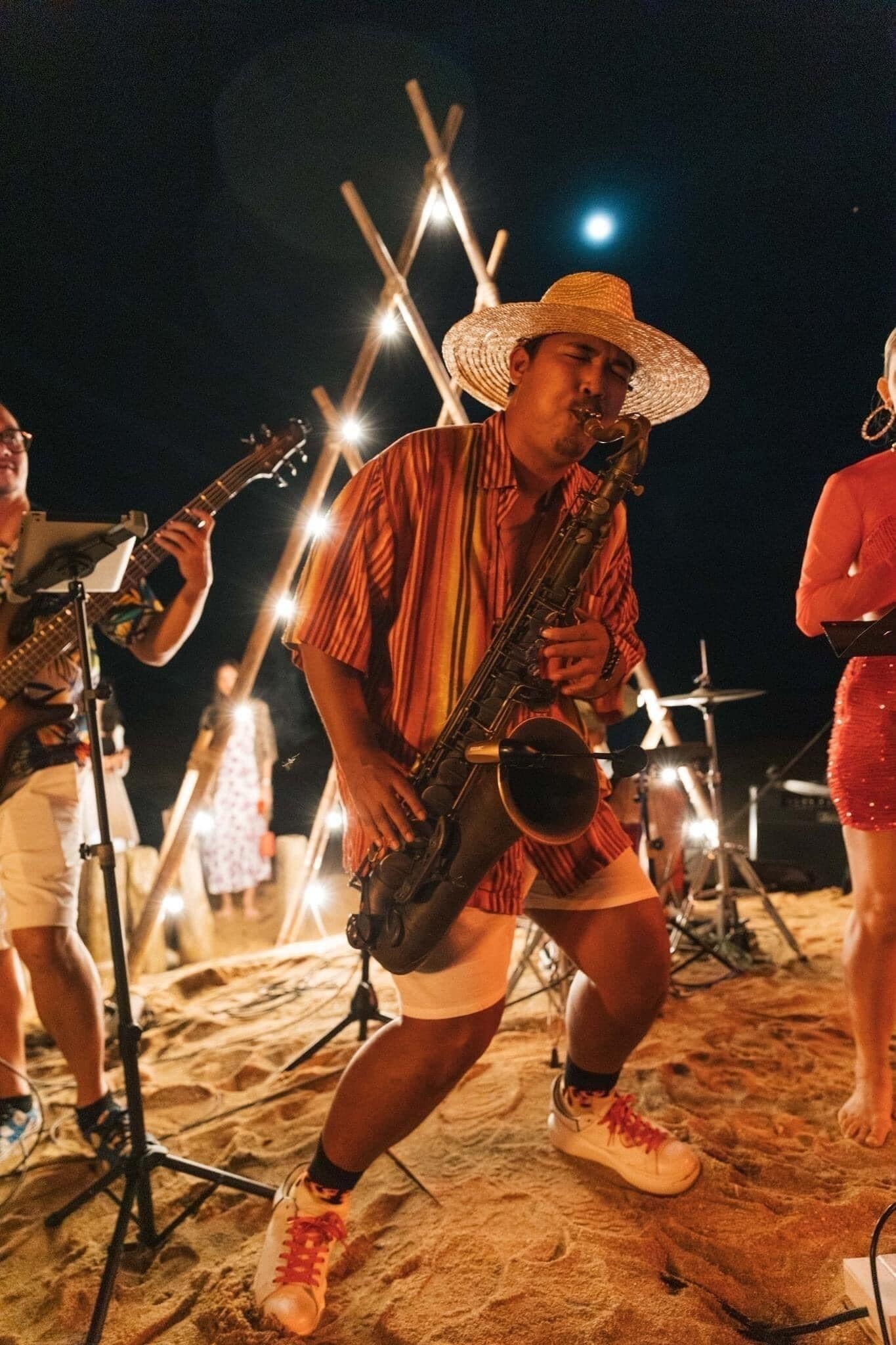 A person playing a saxophone on a sandy beach at night.
