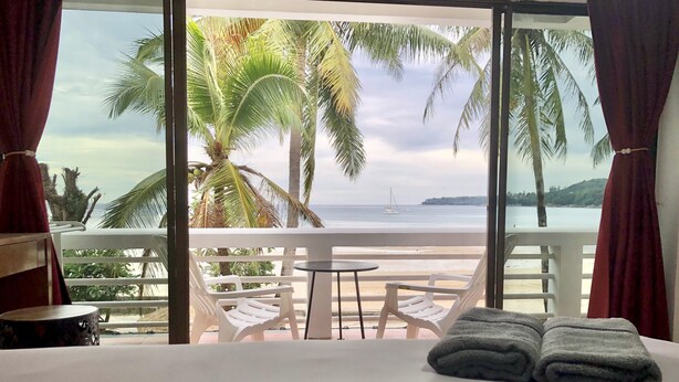 A hotel room with a balcony, white plastic chairs, a small round table, and a bed with two folded towels. - Benjamin Resort (Kamala)