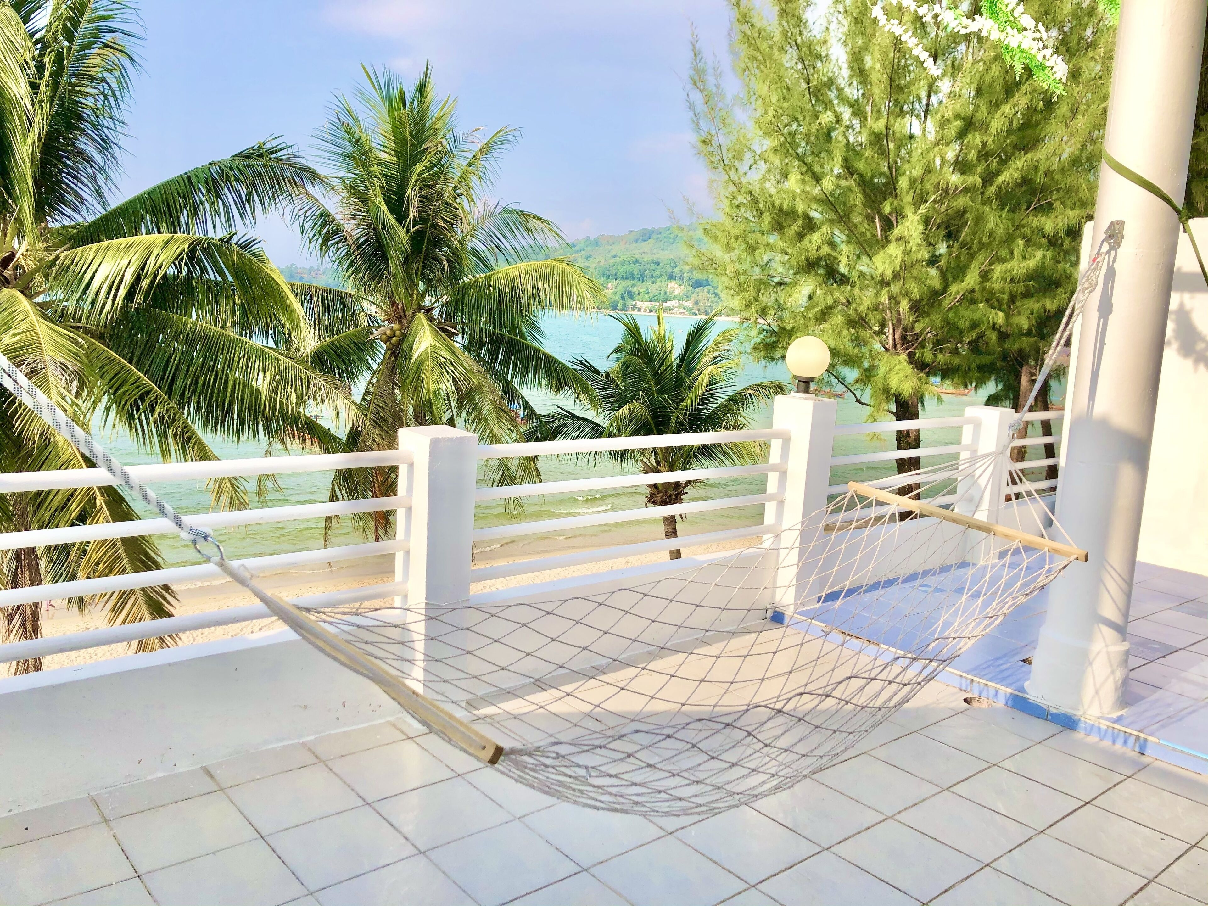 Un balcone con un'amaca, ringhiera bianca e vista sul mare e palme.