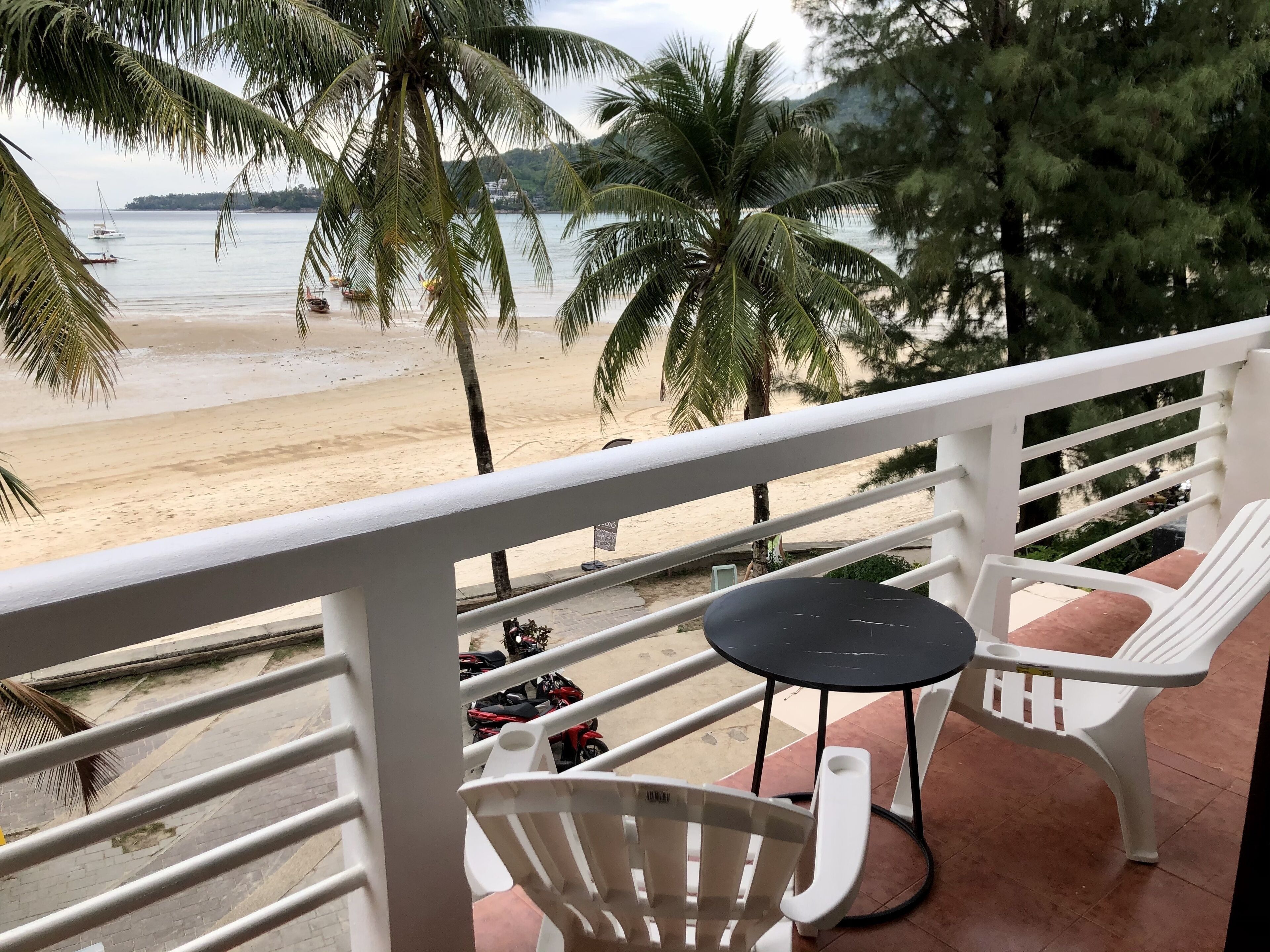 Un balcón con vista a una playa, palmeras y una mesa con sillas.