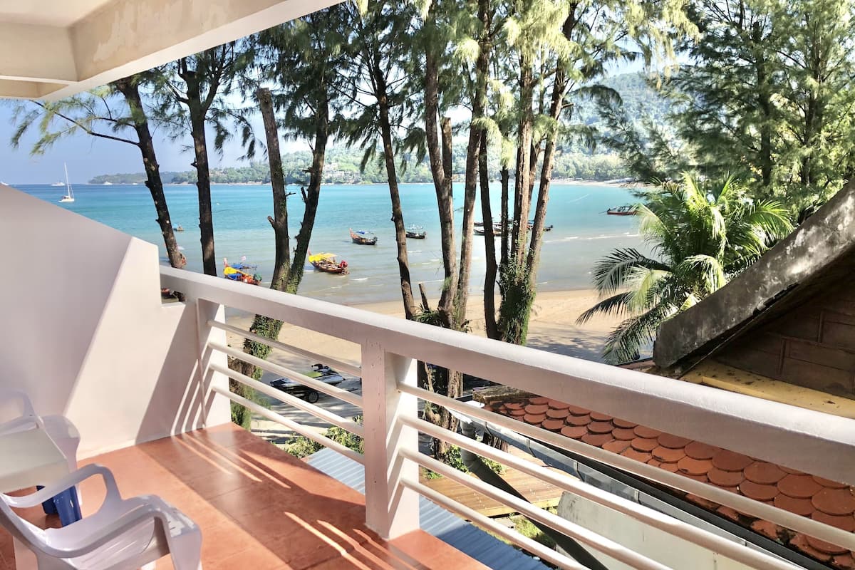 A balcony with a view of a beach, palm trees, and boats on the water.