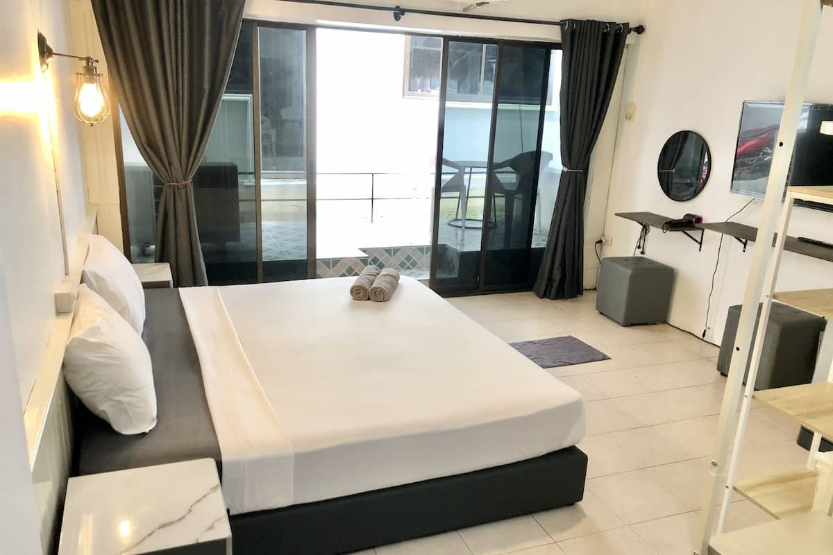 A modern hotel room with a large bed, a balcony with a table and chairs, and a view of the outdoors.
