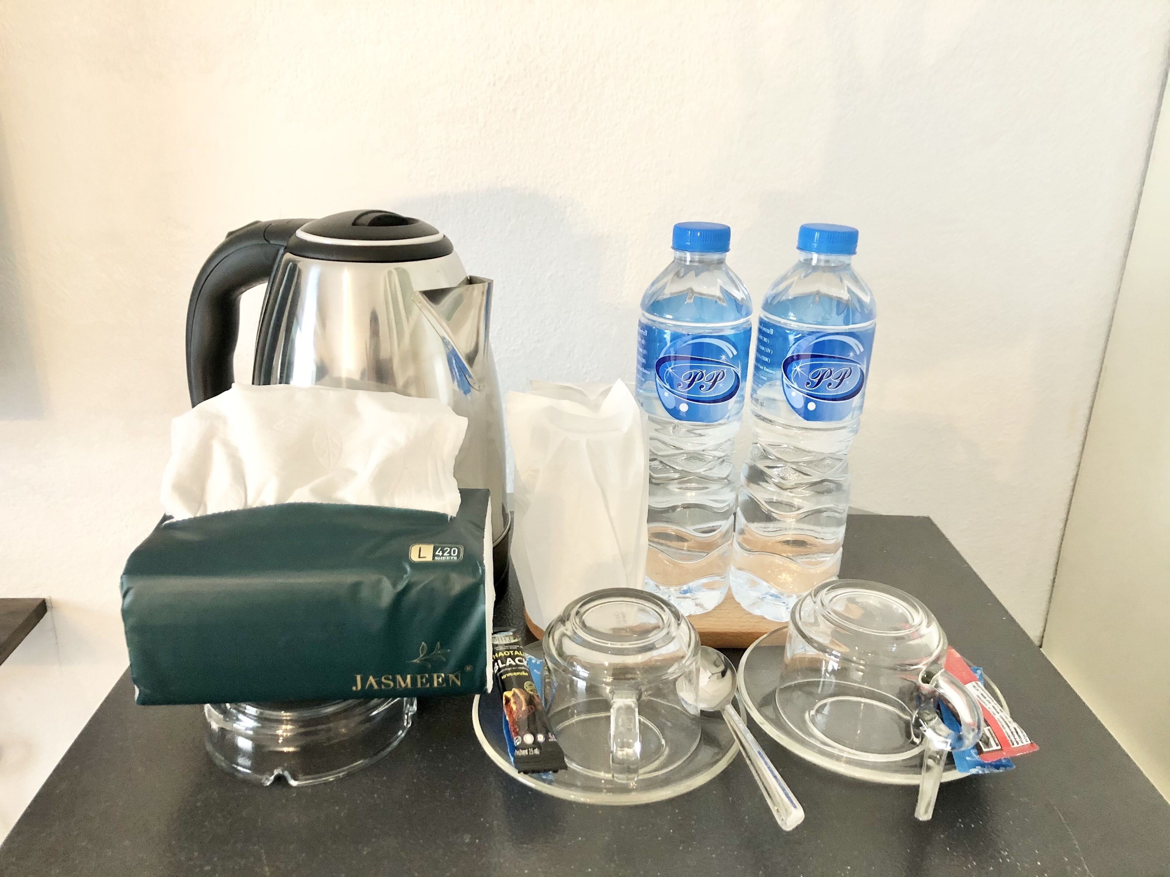 A table with a kettle, two water bottles, a tissue box, and a small tray with a spoon.