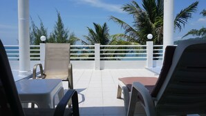 A terrace with white railings, two chairs, a table, and a view of the sea and palm trees. - Benjamin Resort (Kamala)