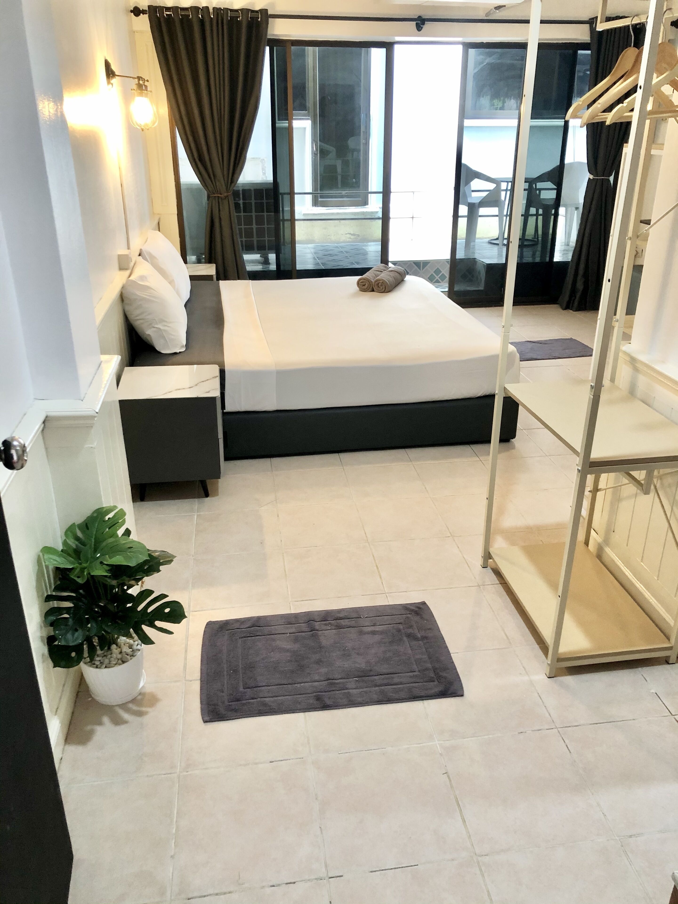 A hotel room with a bed, a small seating area, a potted plant, and a view of the outside.