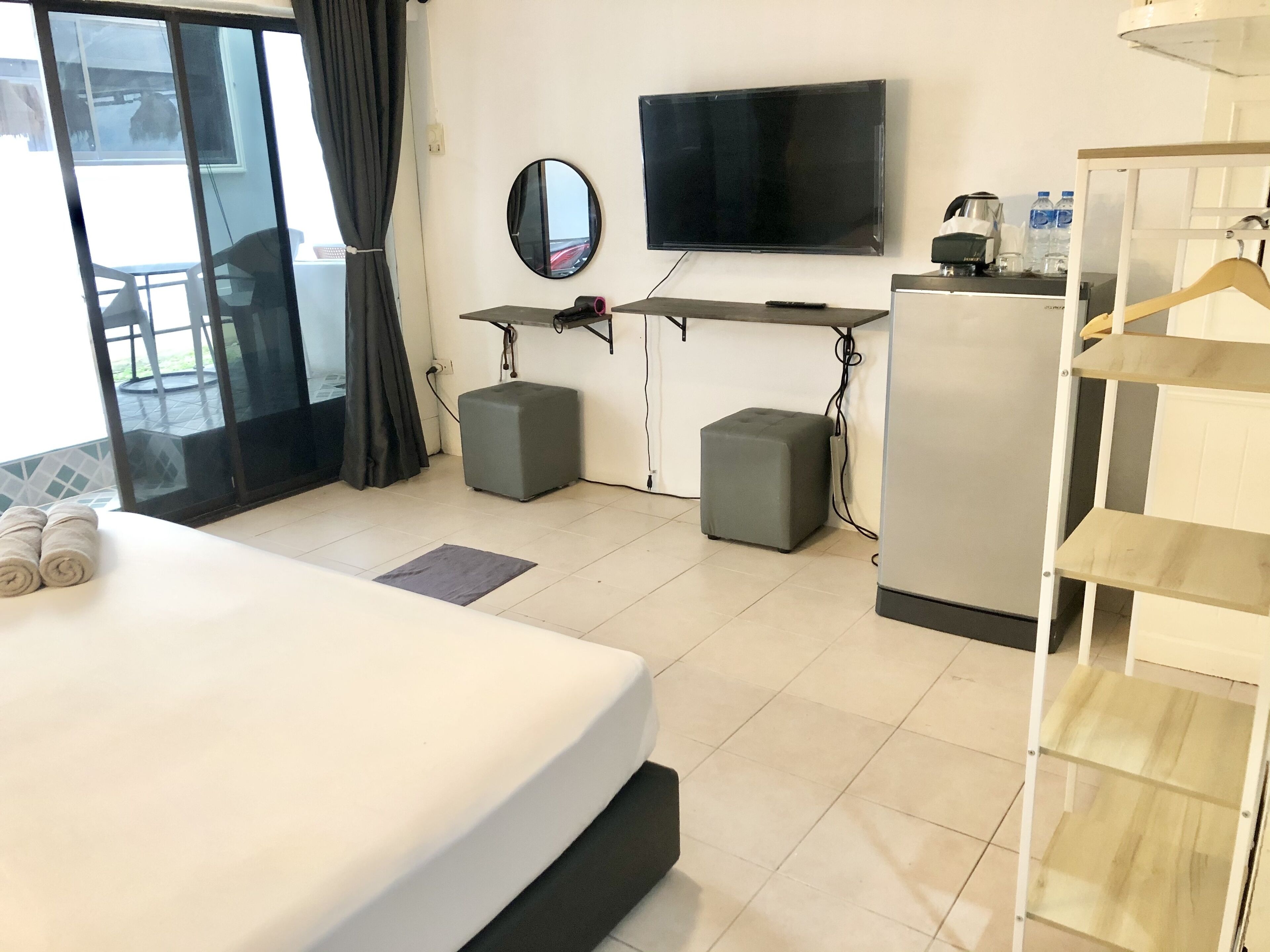 Habitación de hotel con cama, televisor, escritorio, dos otomanas, un espejo y un armario con estantes.