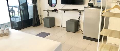 Habitación de hotel con cama, televisor, escritorio, dos otomanas, un espejo y un armario con estantes.