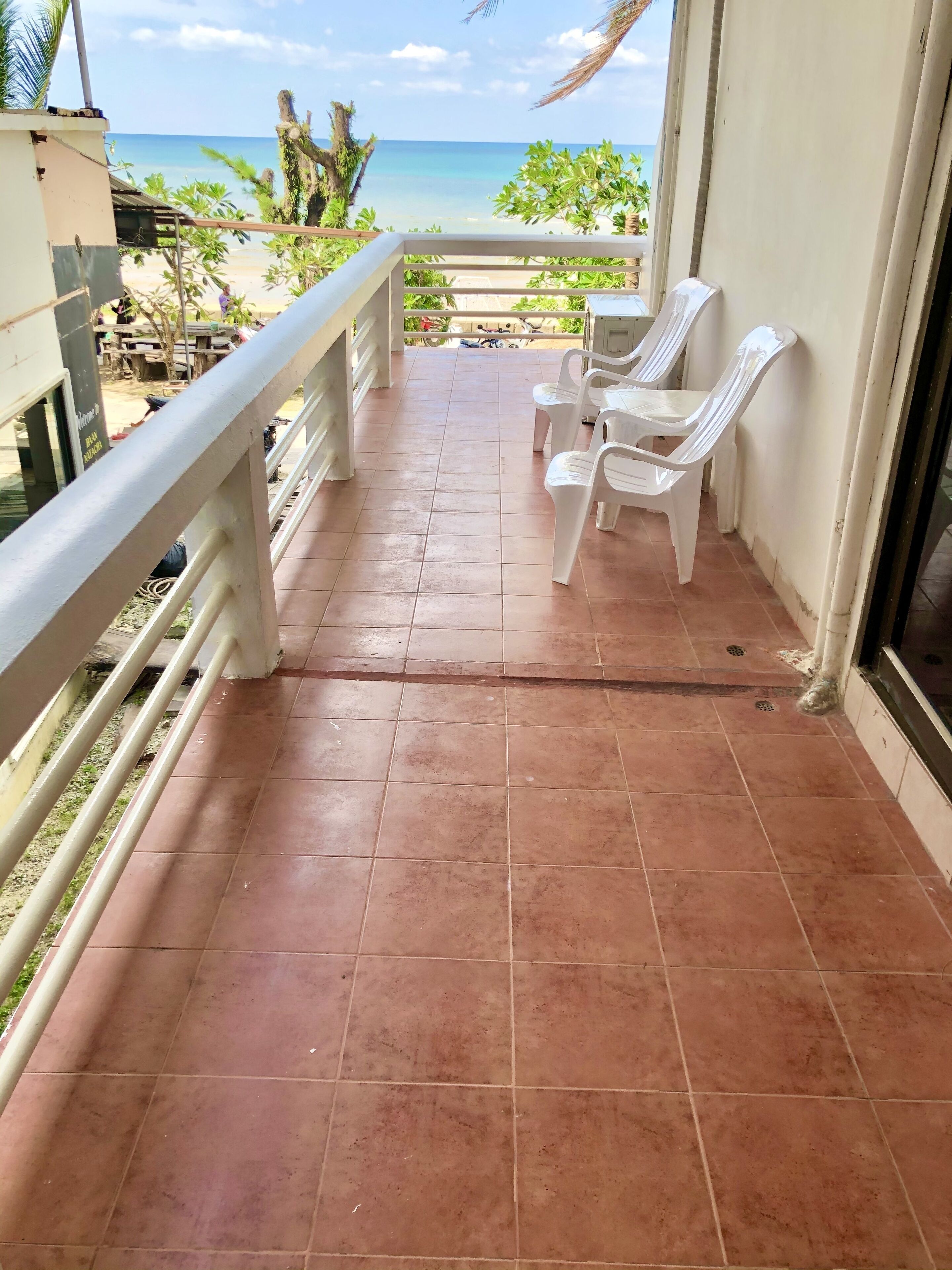Un balcón con suelo de baldosas, sillas de plástico blanco y vista a la playa.