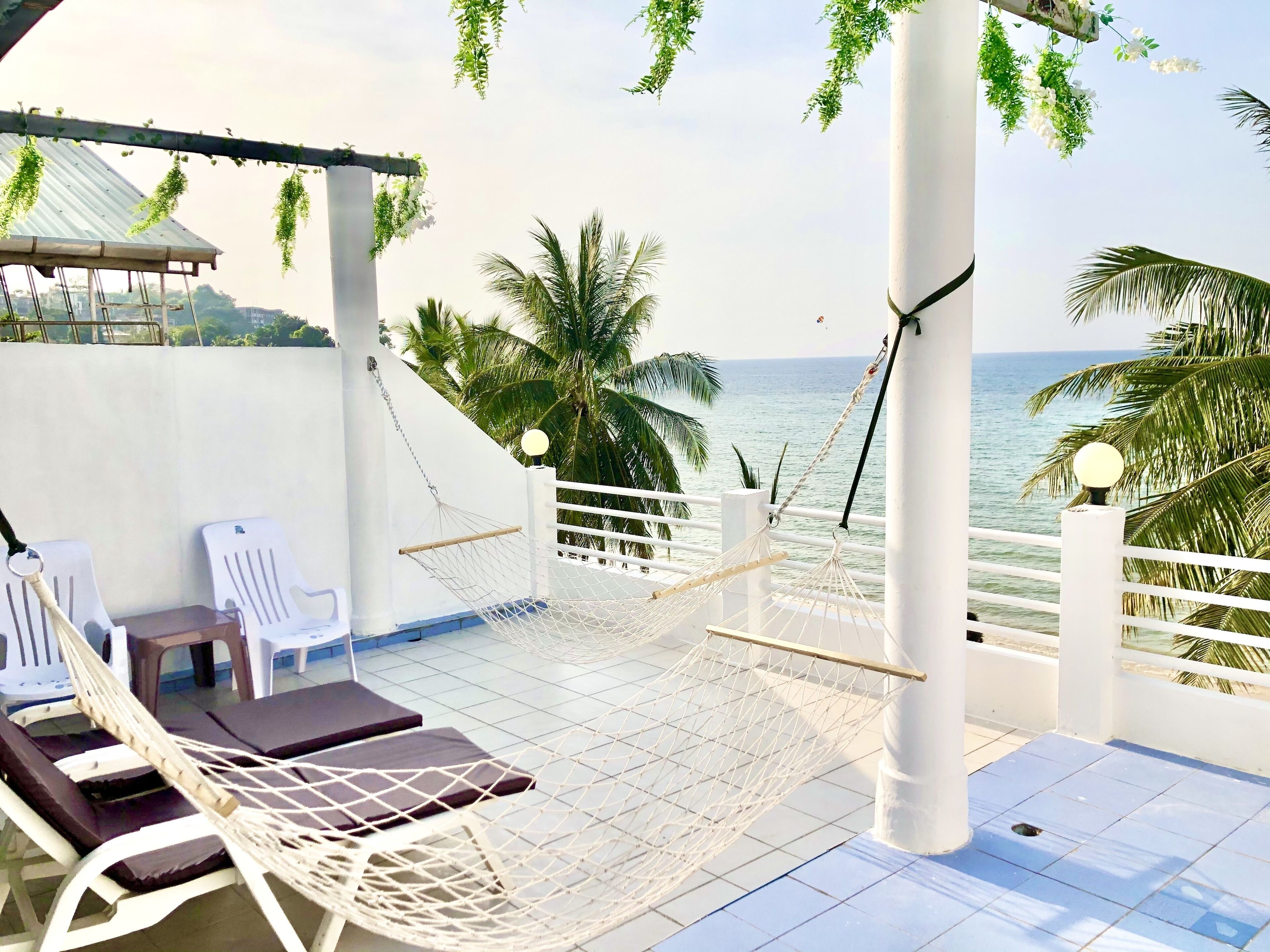 Une terrasse sur le toit, avec des chaises longues blanches, un hamac et une vue sur la mer.