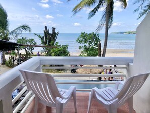 Un balcón con dos sillas de plástico blanco, vista a la playa y palmeras.