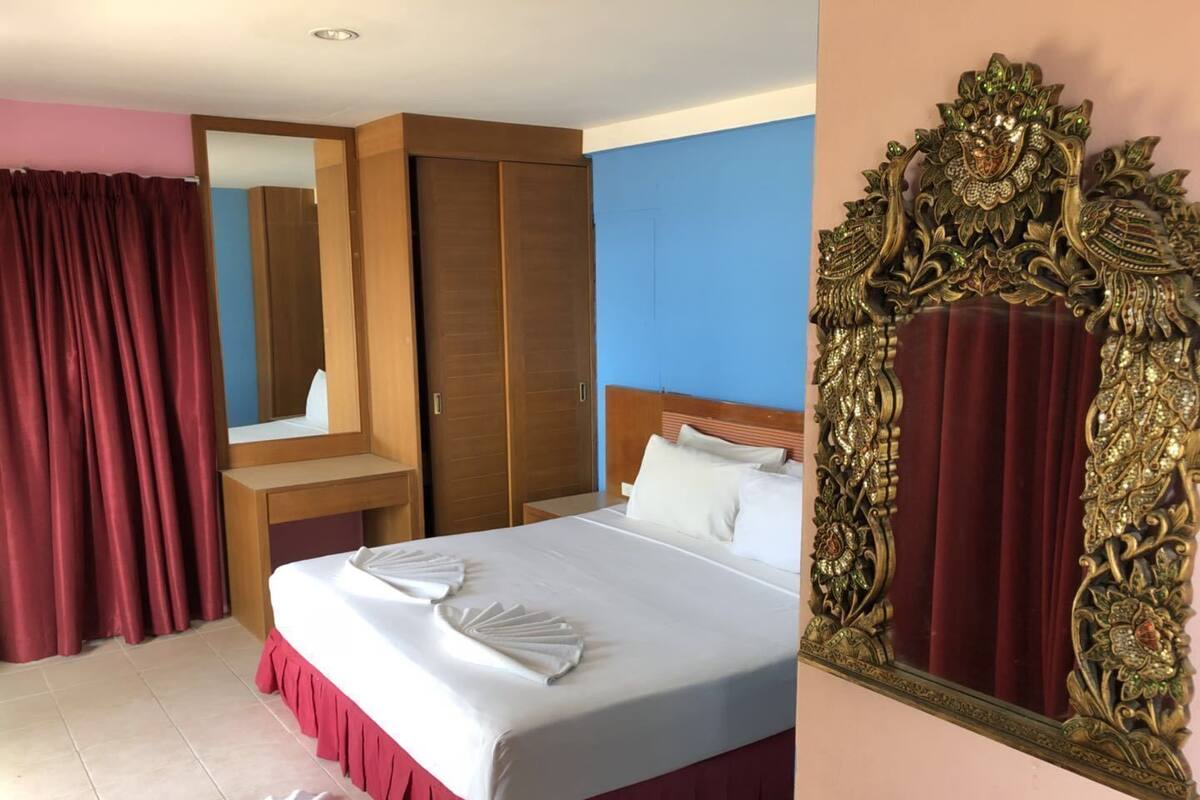 A hotel room with a bed, a wooden wardrobe, a mirror, and a decorative mirror frame.