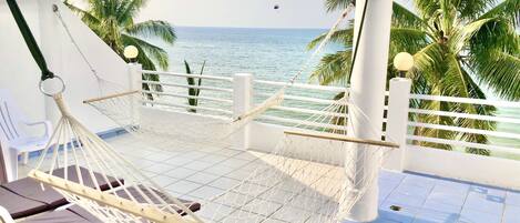 A hammock chair on a balcony with a view of the sea and palm trees.