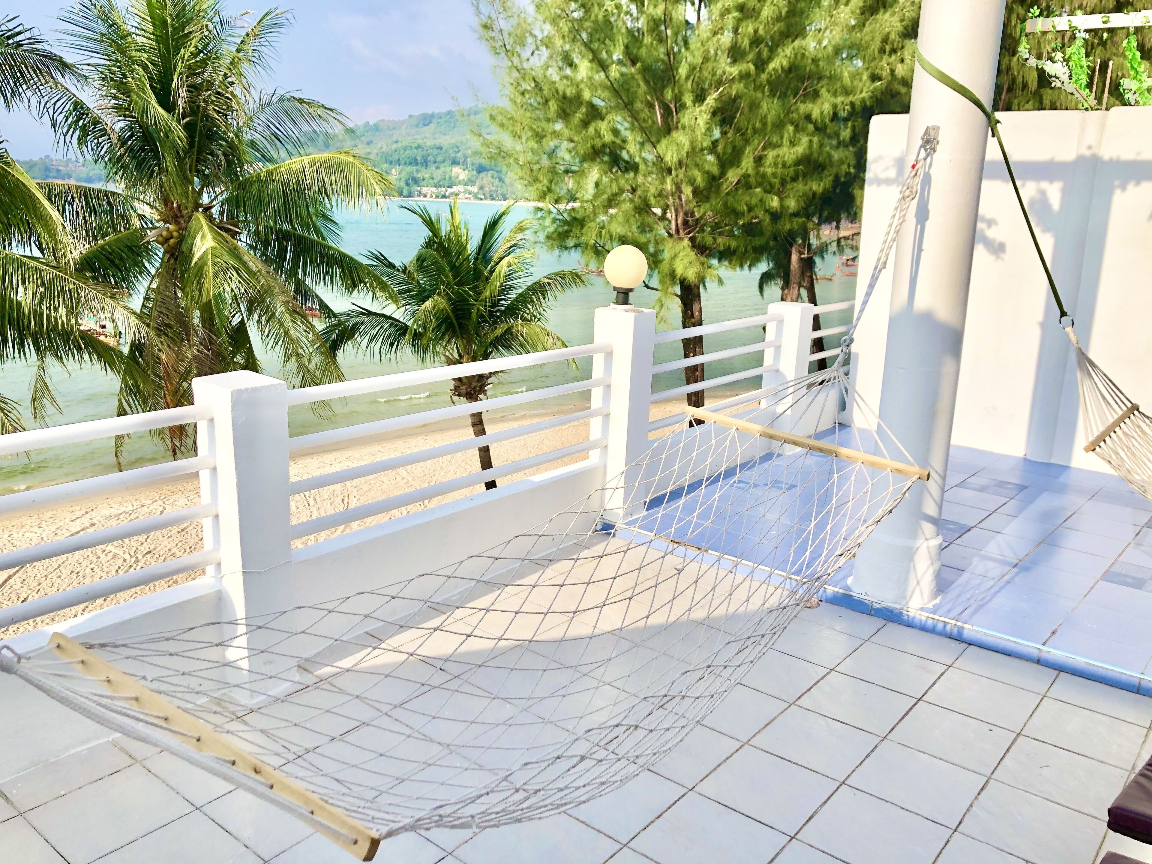 Una hamaca en una terraza con baldosas, con vista a una playa, palmeras y el mar.