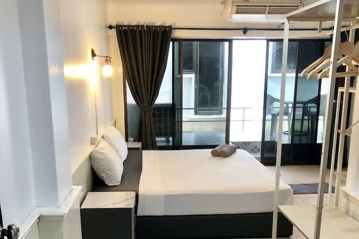 A modern hotel room with a large bed, a bedside table, a small desk, a potted plant, and a view of the balcony.