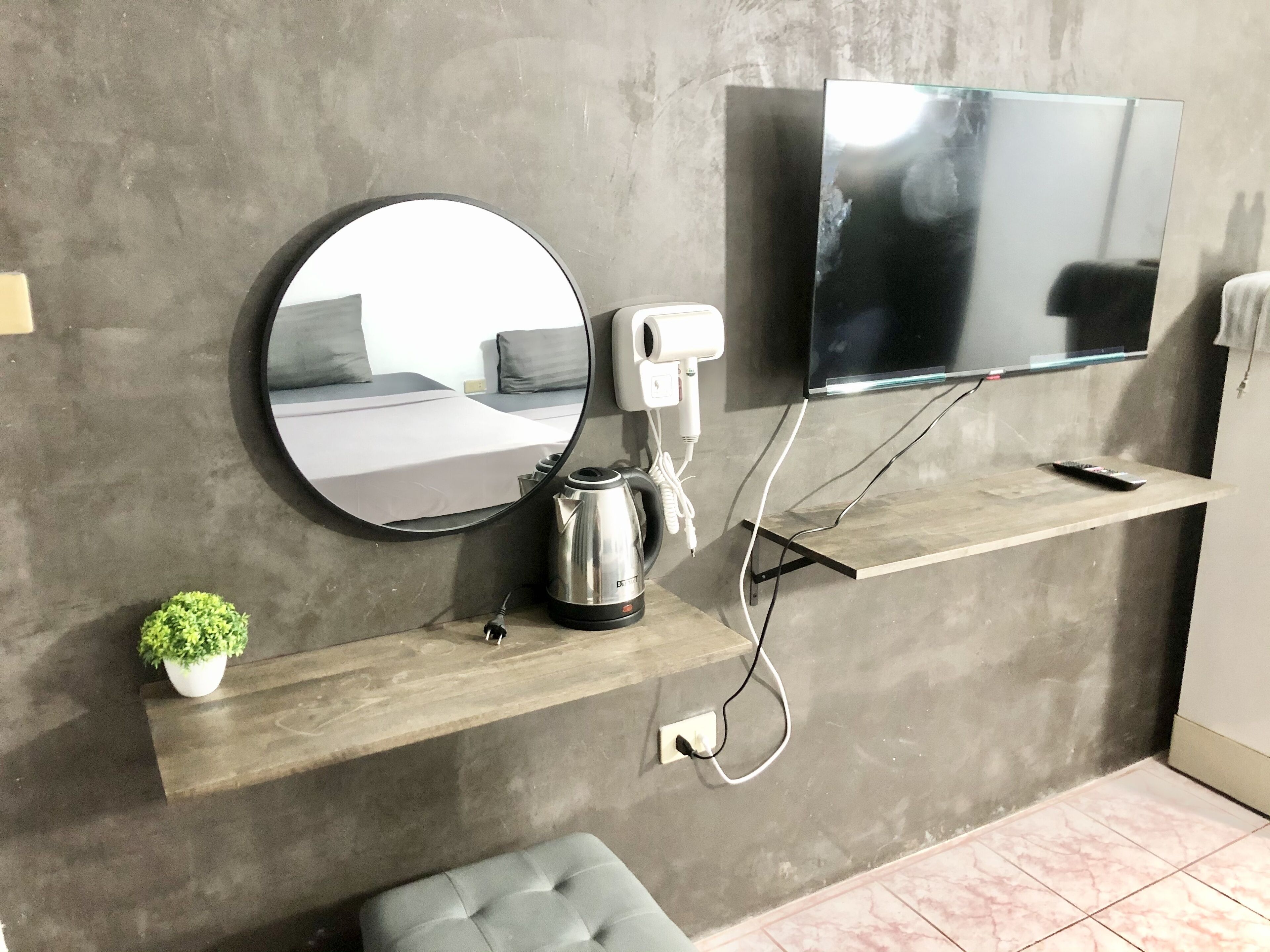 A modern room with a mounted TV, a round mirror, a small potted plant, a kettle, and a charging station.