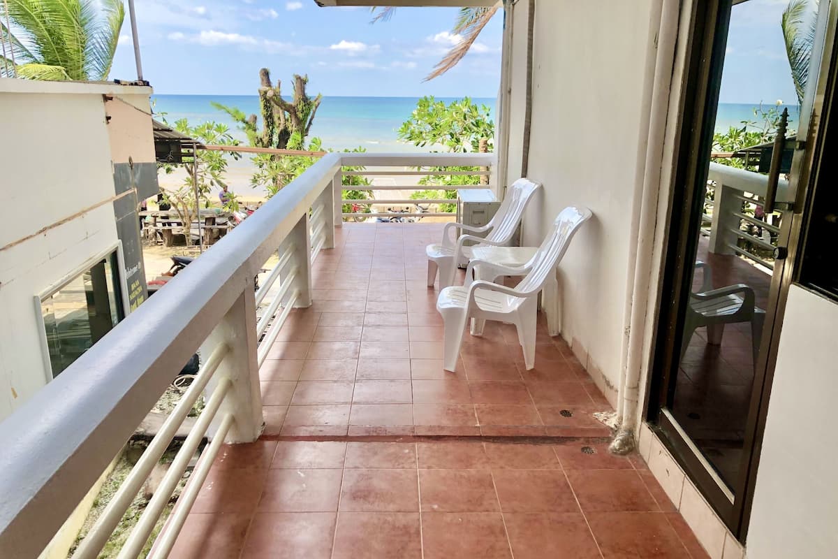 A balcony with a view of the beach, white plastic chairs, and a tiled floor.