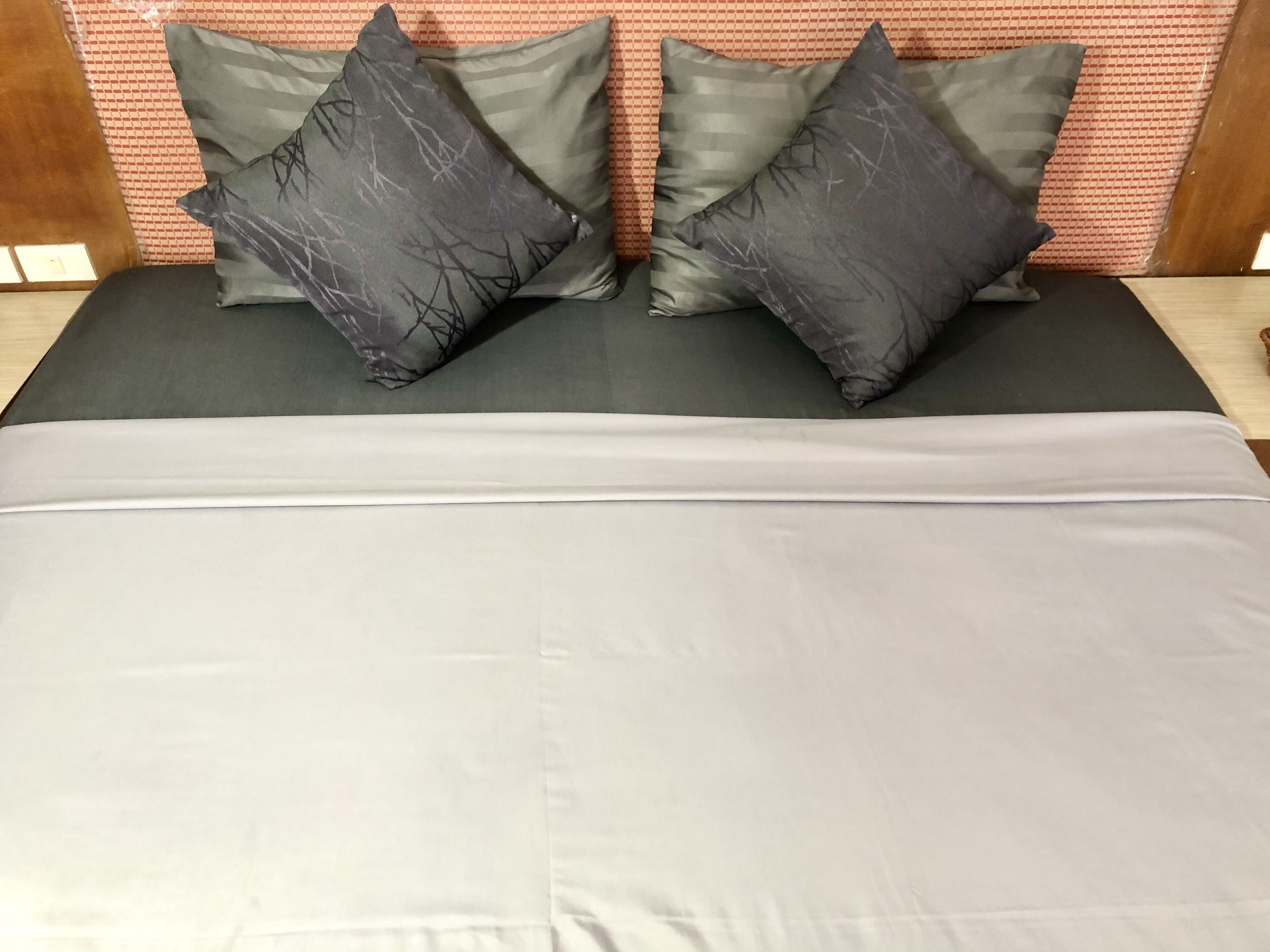 A bed with a grey mattress and two grey pillows with tree branch patterns.