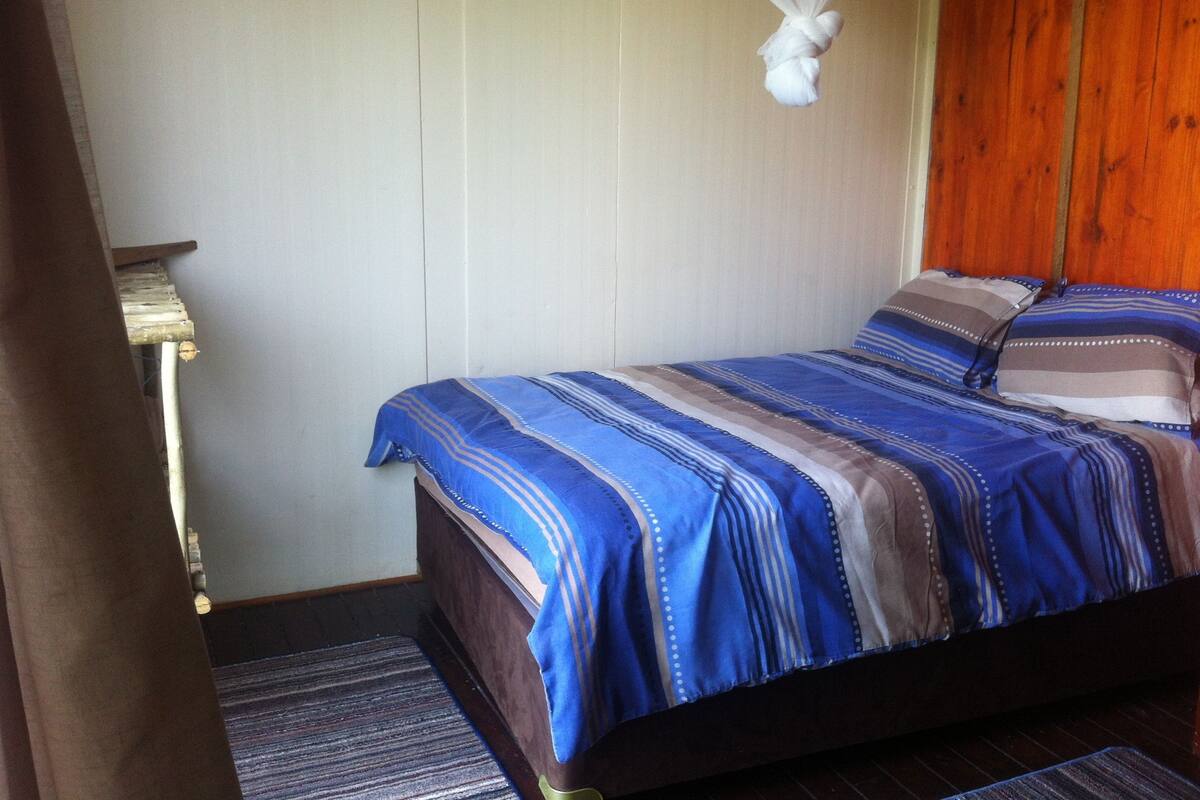 A neatly made bed with striped bedding, a bedside lamp, and a wooden headboard.