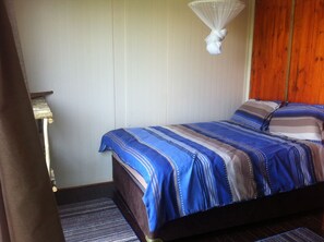A neatly made bed with striped bedding, a bedside lamp, and a wooden headboard. - Delta Belle Boathouse (Shakawe)