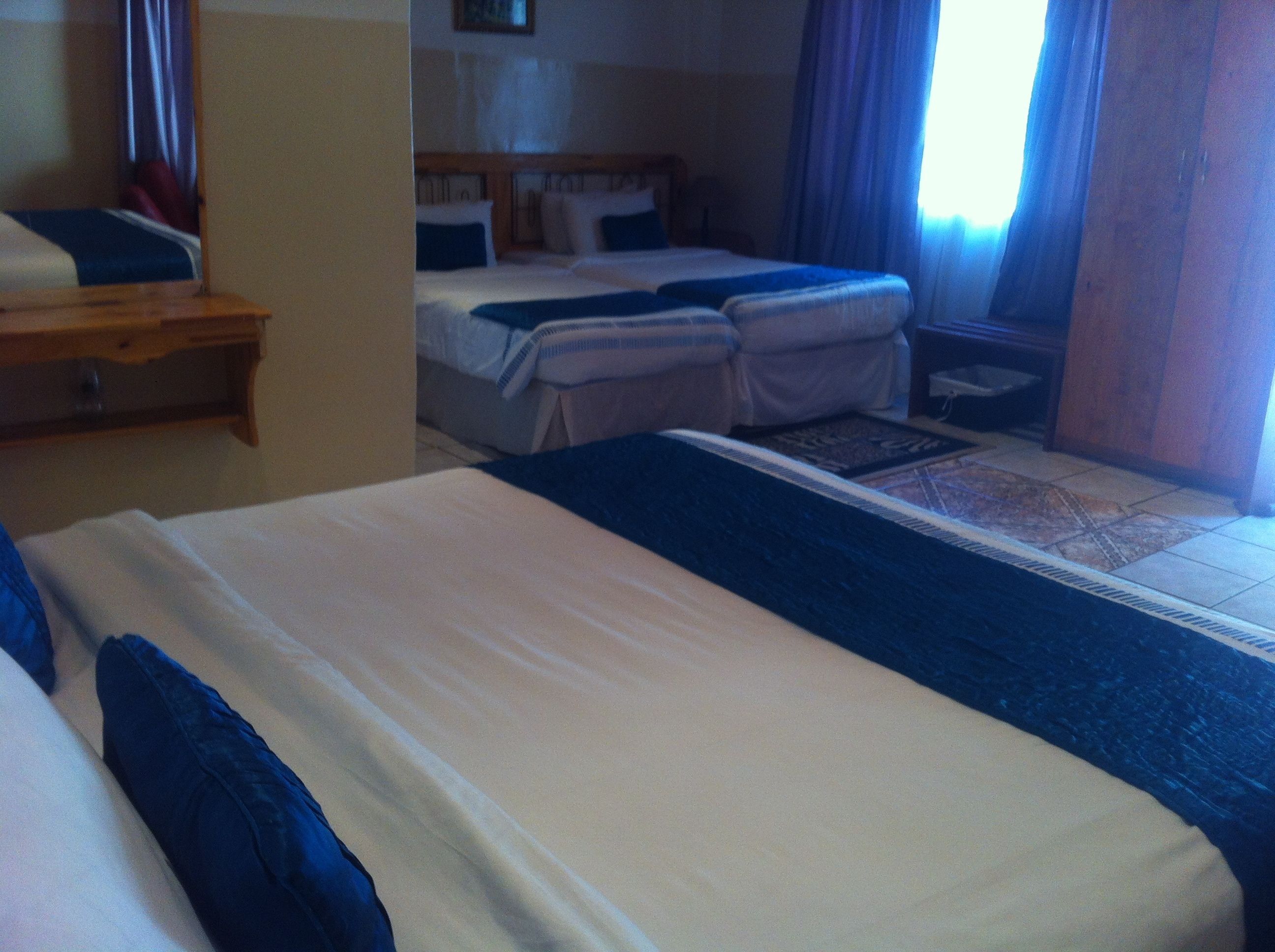 A hotel room with two beds, a wooden headboard, a small table, and a window with curtains.