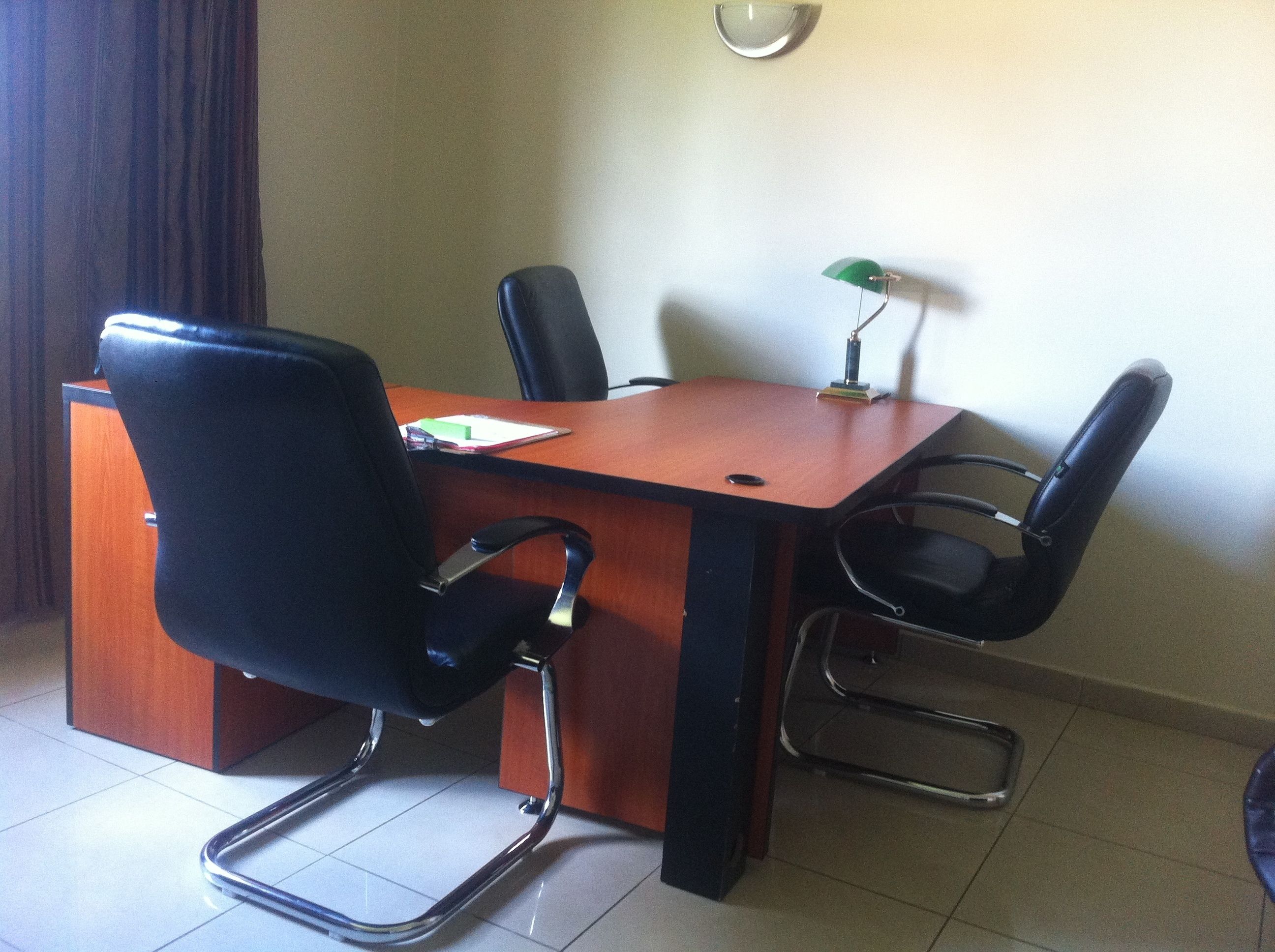 A conference room with a wooden table, four black chairs, a green desk lamp, and a whiteboard.