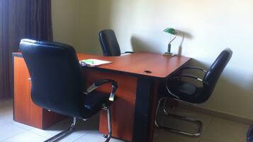 A conference room with a wooden table, four black chairs, a green desk lamp, and a whiteboard.