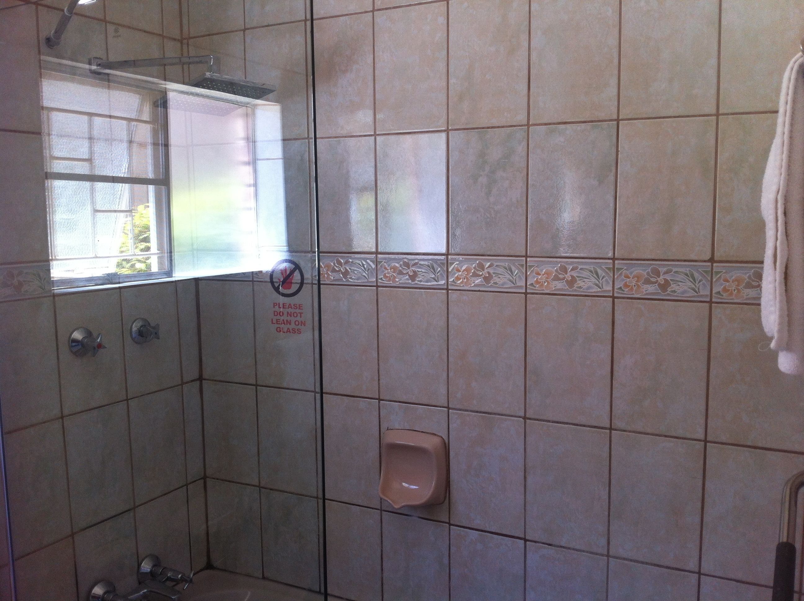 Un área de ducha con paredes de azulejos, una puerta de cristal, un secador de manos y una toalla colgada en la pared.