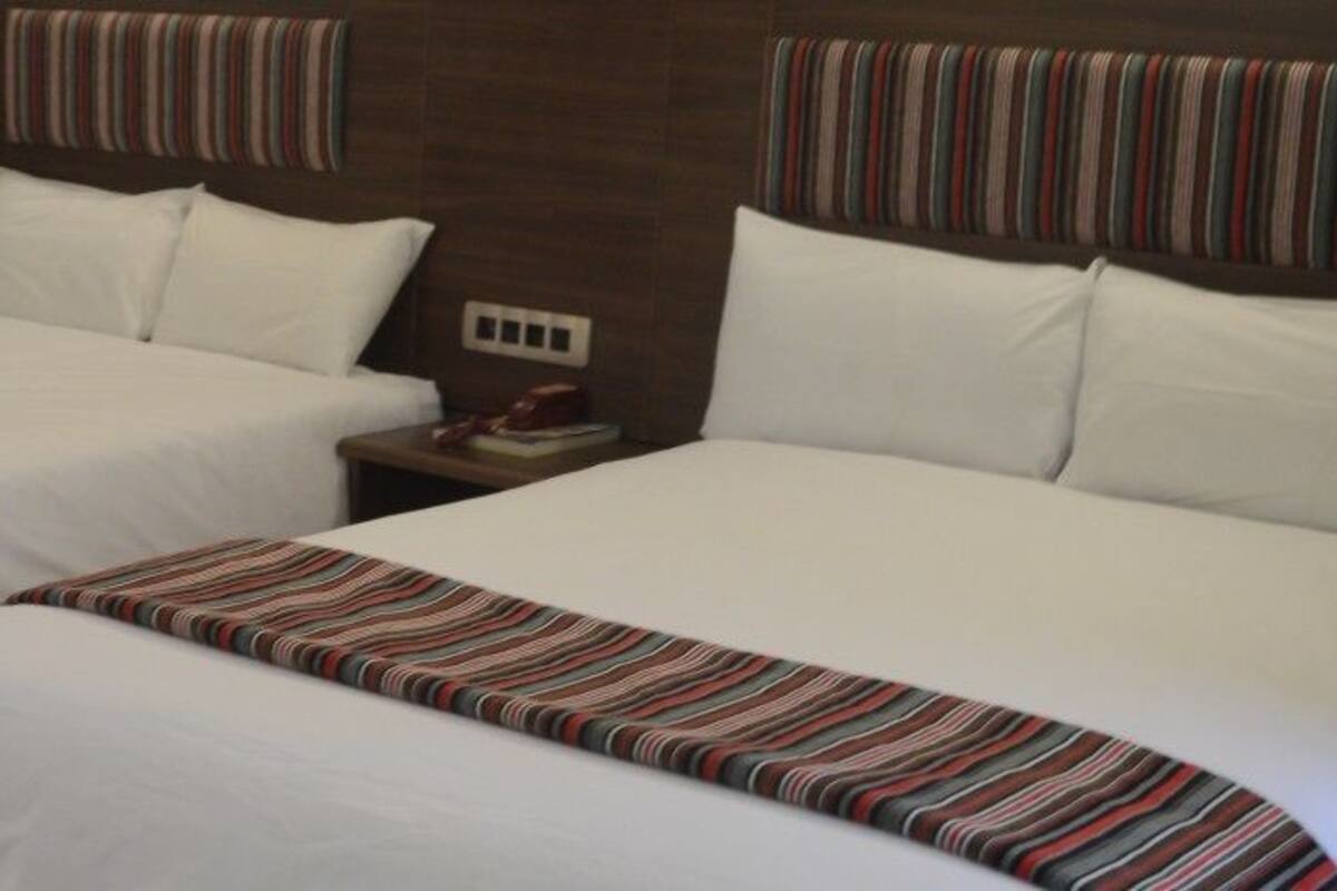 A hotel room with two beds, each with a striped bedspread and white pillows. There is a brick wall and a window with curtains.