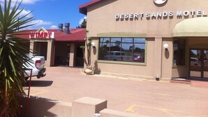 The Desert Sands Motel with a red roof and a sign featuring a palm tree and desert landscape. - Desert Sands Motel (Palapye)