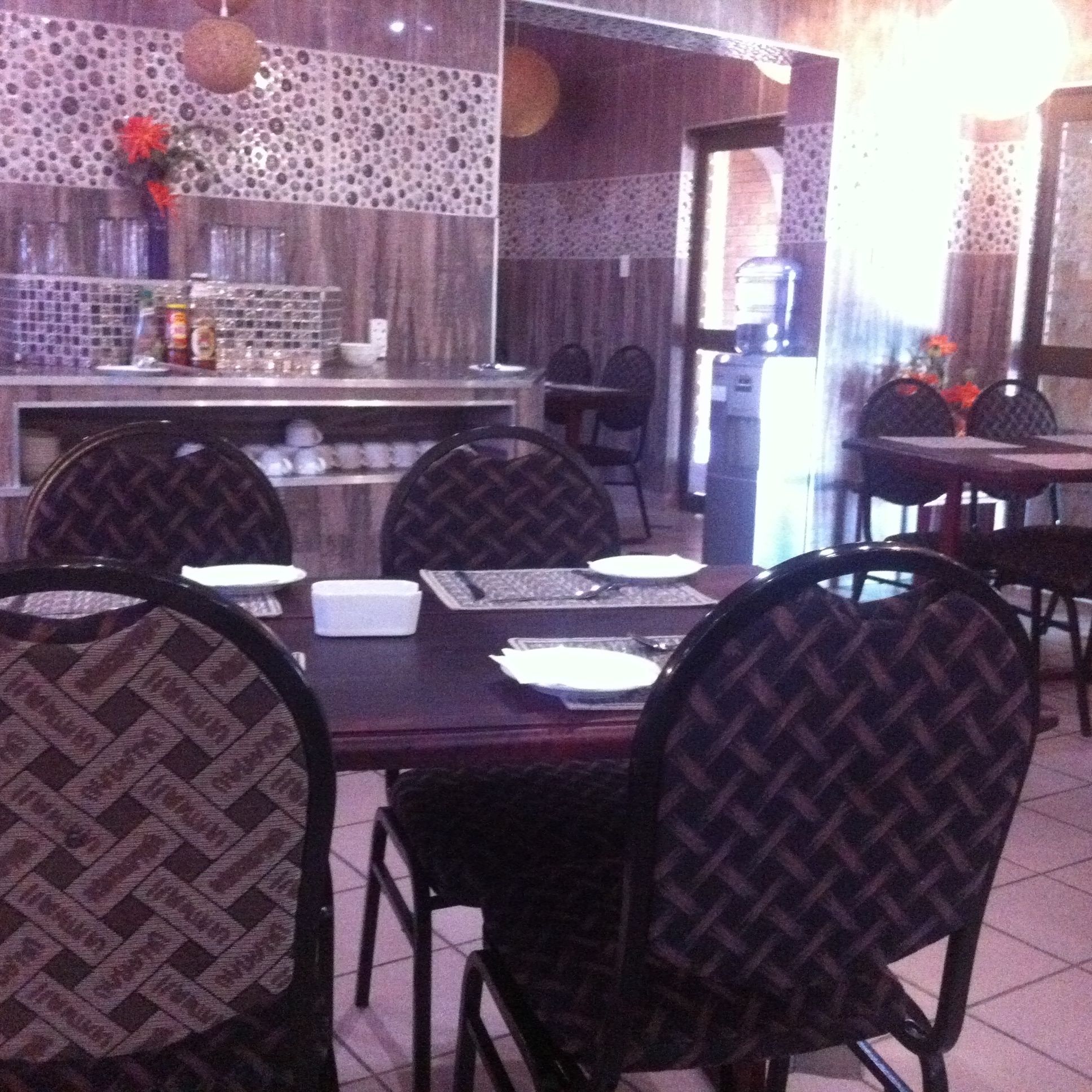 L’intérieur d’un restaurant présente un mur recouvert de carreaux, un bar et plusieurs tables avec des chaises.