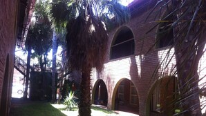 A courtyard with a palm tree, brick building with arched doorways, and a staircase. - Desert Sands Motel (Palapye)