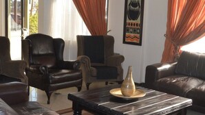 A living room with leather sofas and armchairs, a coffee table, and a large potted plant. - Desert Sands Motel (Palapye)