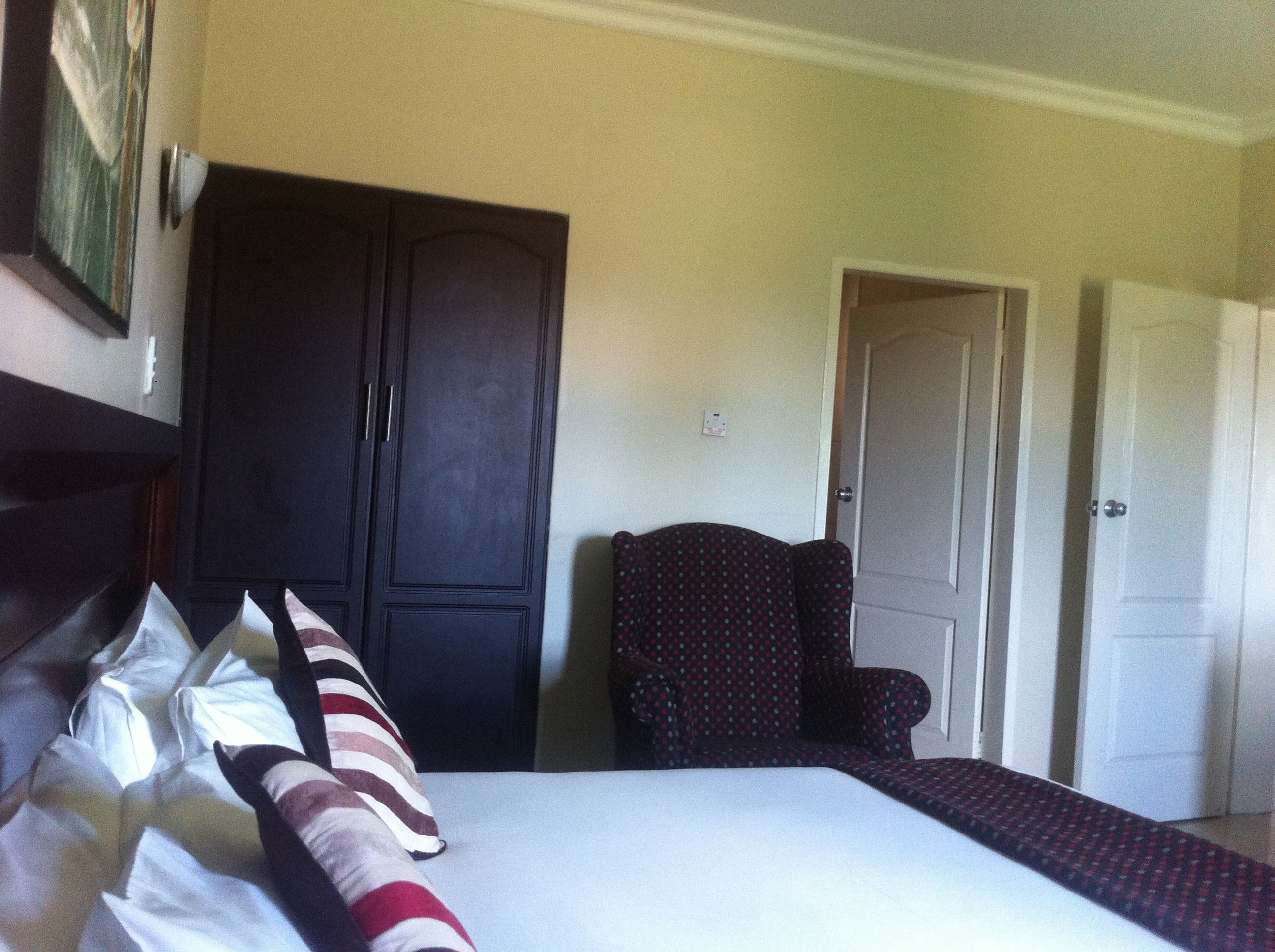 A bedroom with a bed, a dark wardrobe, a patterned armchair, and a door.