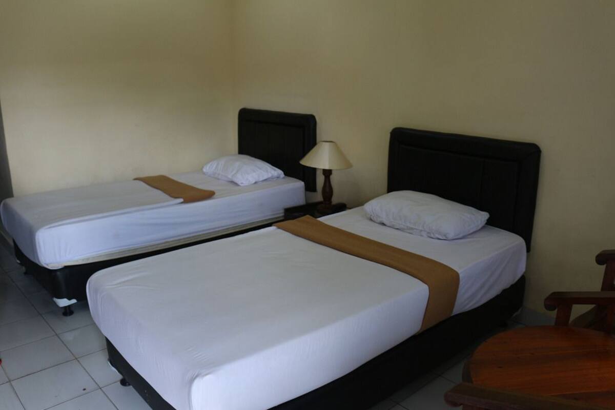 Two single beds with wooden headboards and white bedding, a small table with a lamp, and a wooden chair.