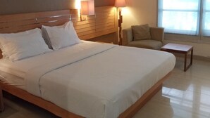 A neatly made bed with white linens, a wooden headboard, and bedside lamps. - Serayu Hotel Timika (Timika)
