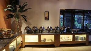 A buffet setup with multiple serving stations, a potted plant, and a window view. - Serayu Hotel Timika (Timika)