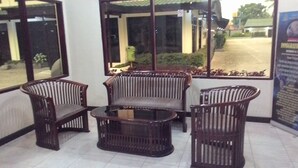 A seating area with three wicker chairs and a small table, a window with a view of the outside, and a poster on the wall. - Serayu Hotel Timika (Timika)
