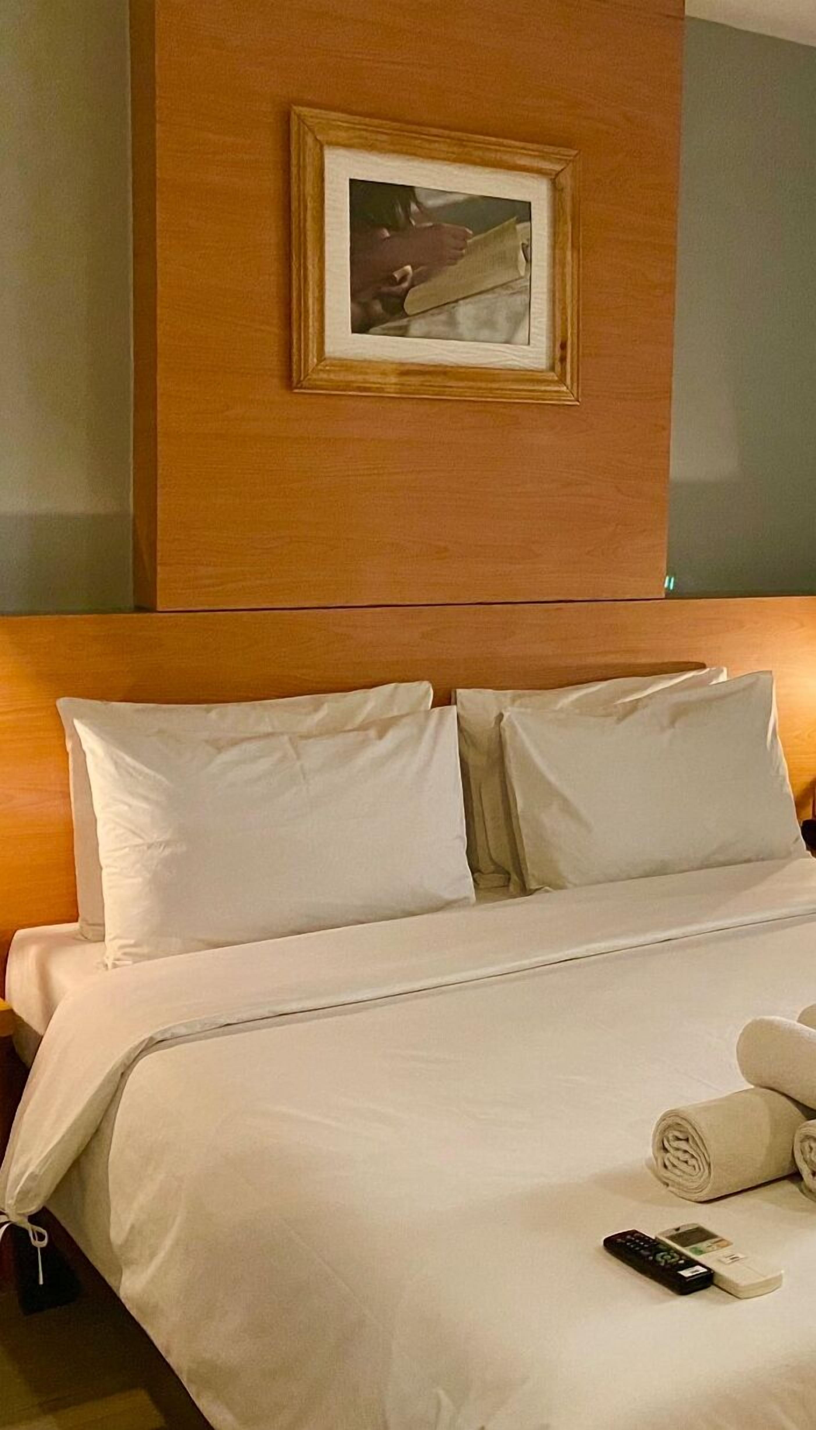 A hotel room with a neatly made bed, a framed picture on the wall, and a remote control on the bed.