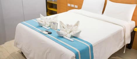 A neatly made bed with white linens and a blue-striped bedspread, a bedside table with a lamp, and a sign indicating the room is for VIP guests.