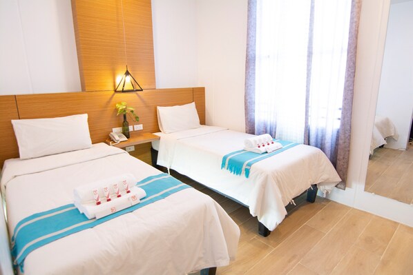 Habitación de hotel con dos camas, cabecero de madera, lámpara de pared, teléfono y ventana con cortinas.