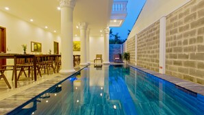 An indoor swimming pool with a long, narrow design, flanked by white columns and a brick wall on one side. - Terrace Villa Hoi An (Da Nang)