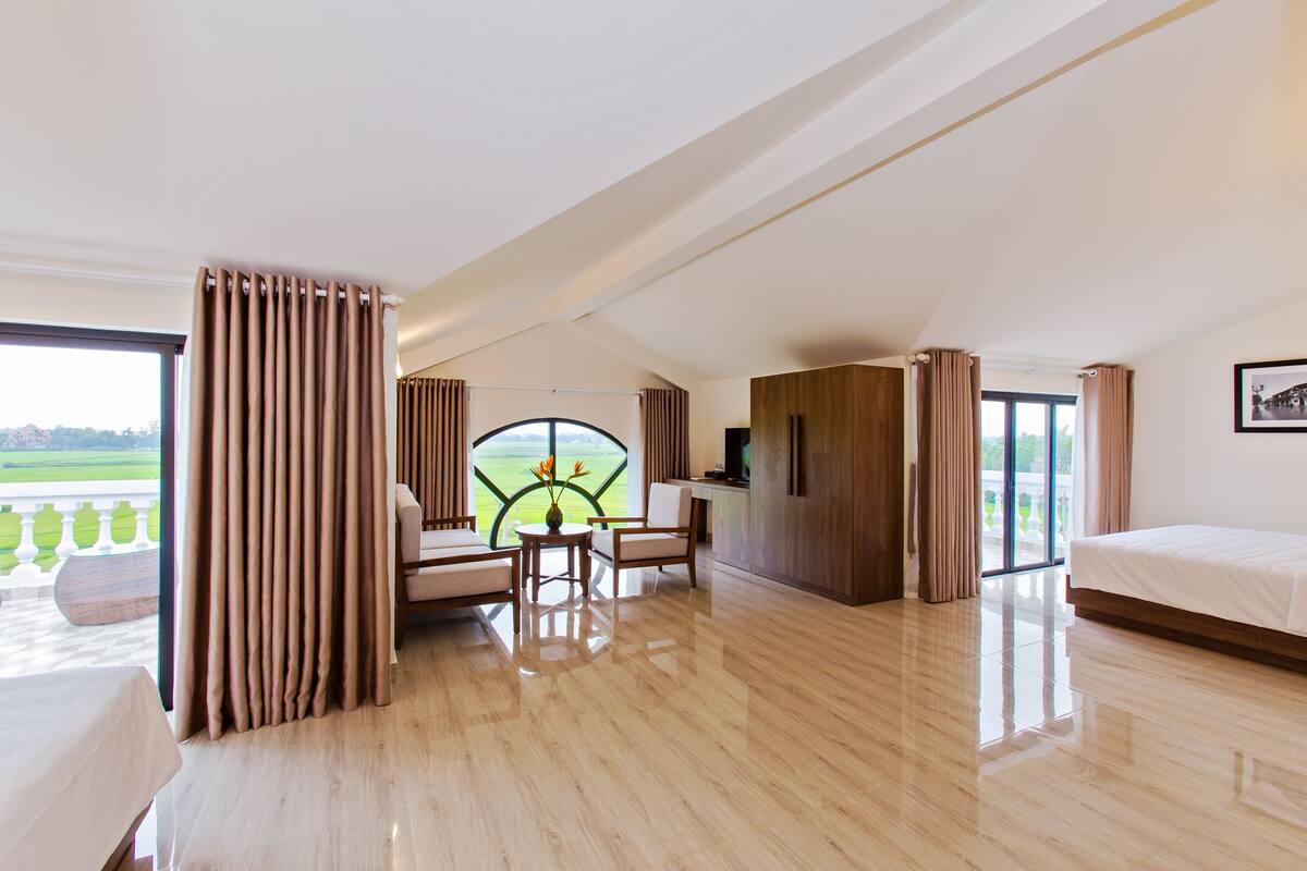 A spacious room with a large window, a bed, a desk, and a view of a green landscape.